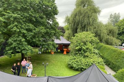 Parking en gravier entouré d'arbres et de bâtiments en briques sous un ciel partiellement nuageux.