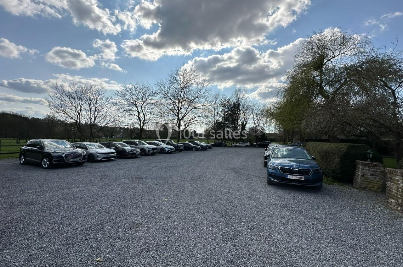 Parking extérieur avec plusieurs voitures stationnées sur un sol en gravier, entouré d'arbres et sous un ciel partiellement…