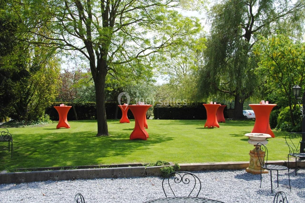Tables hautes rouges disposées sur une pelouse verte, entourées d'arbres et de mobilier de jardin en métal.