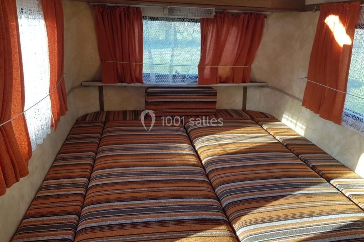 Intérieur d'une caravane avec un lit convertible en tissu rayé orange et marron, entouré de rideaux assortis.