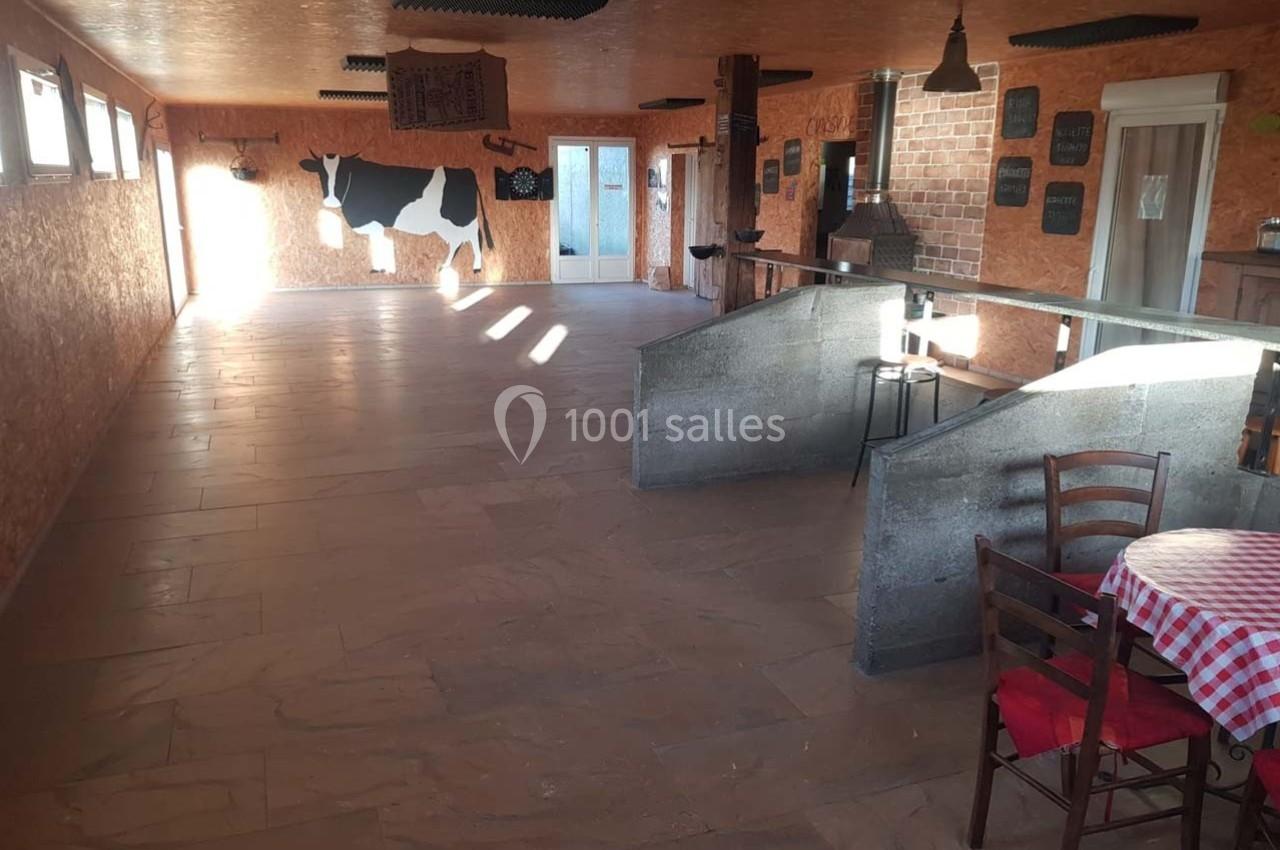 Salle rustique avec murs en bois et briques, décorée d'une silhouette de vache, tables et chaises en bois.