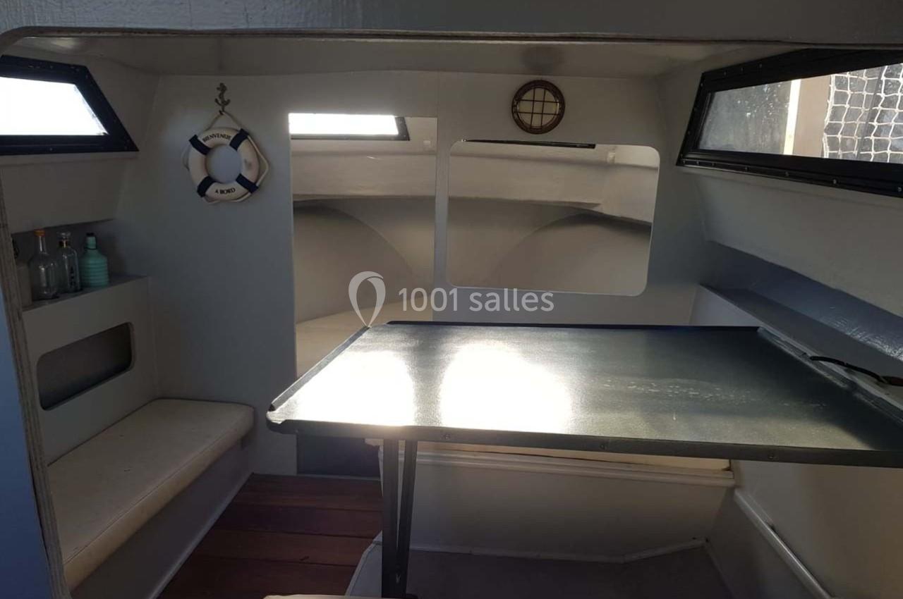 Intérieur d'un petit bateau avec table pliante, banquettes, hublots et décoration marine.