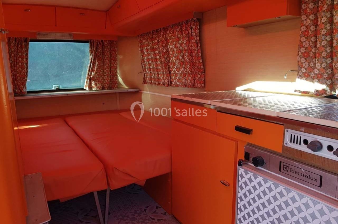 Intérieur d'une caravane vintage avec mobilier orange, rideaux à motifs floraux et un lit convertible.