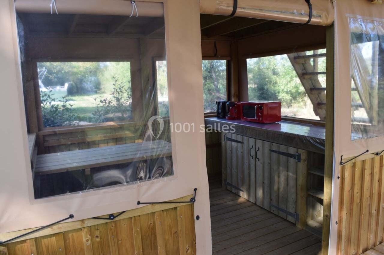 Cuisine extérieure en bois sous une tente avec plan de travail, micro-ondes et vue sur un espace naturel.