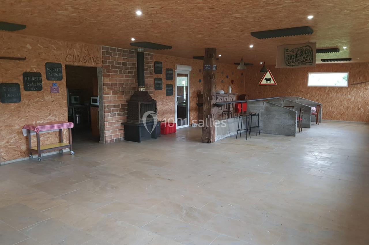 Salle intérieure avec murs en bois, cheminée en briques, bar en béton et mobilier simple dans un espace ouvert.