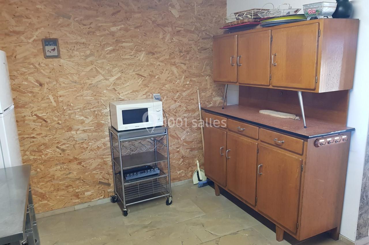 Cuisine simple avec un meuble en bois, un micro-ondes sur un chariot métallique et des ustensiles sur l'étagère.
