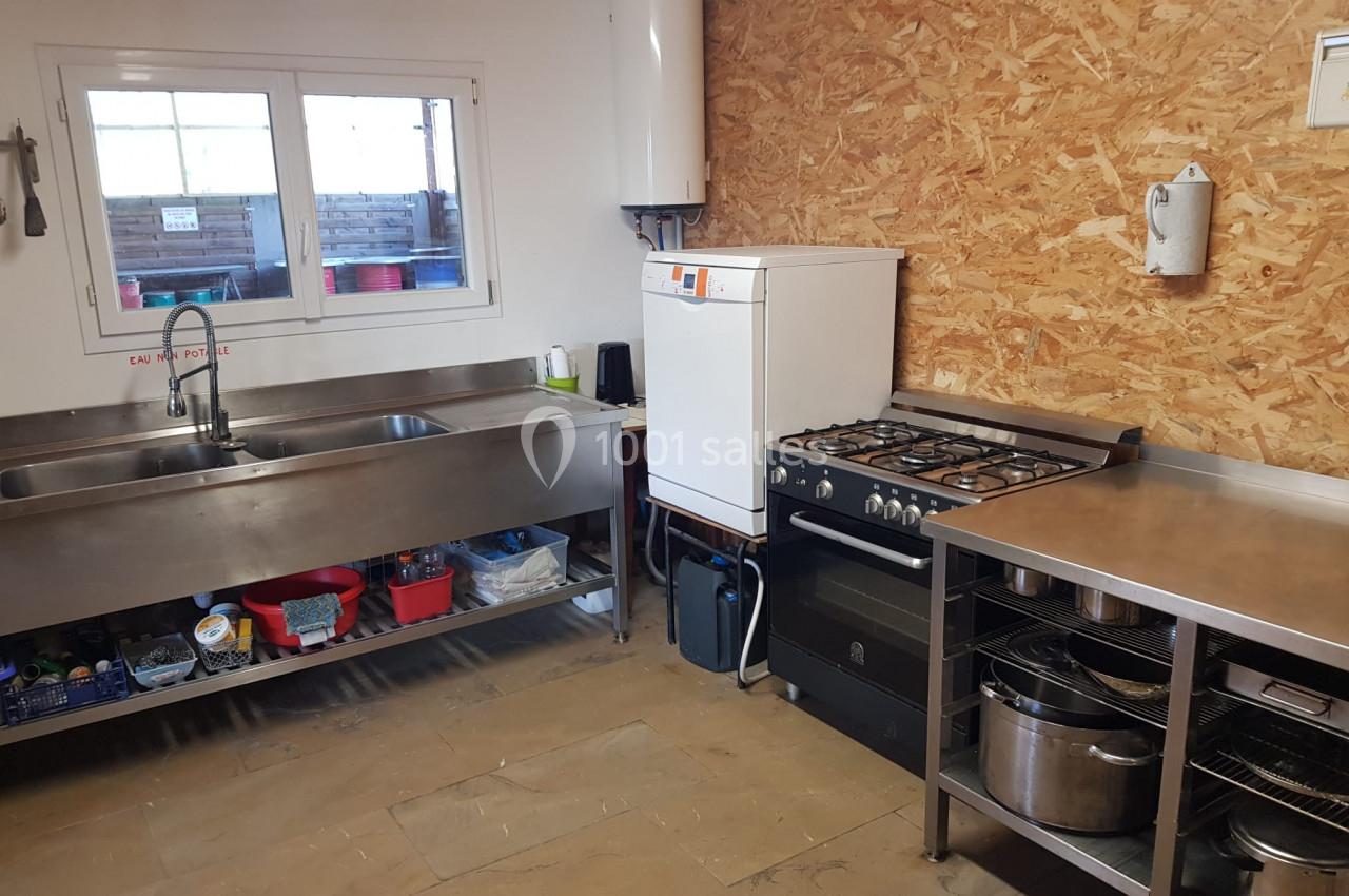 Cuisine équipée avec évier double, gazinière, chauffe-eau mural et étagères de rangement en métal.