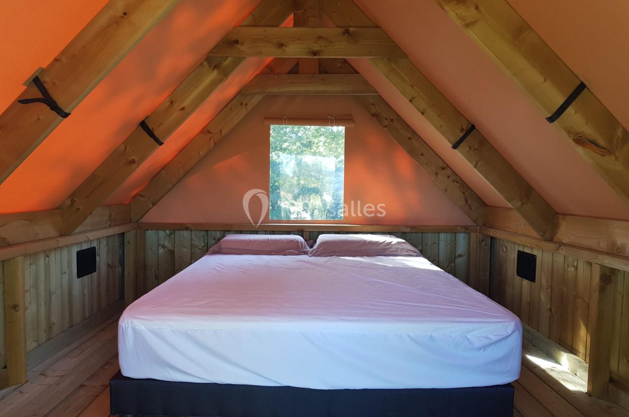 Lit double sous un toit en pente dans une chambre en bois avec une fenêtre laissant entrer la lumière naturelle.