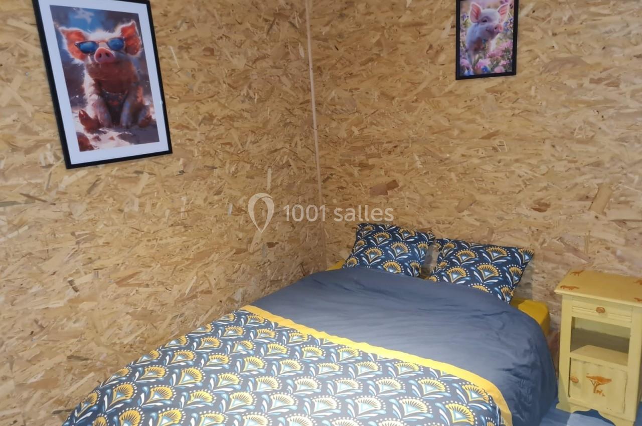 Lit double avec housse de couette colorée, table de chevet jaune et murs en panneaux de bois ornés de cadres.