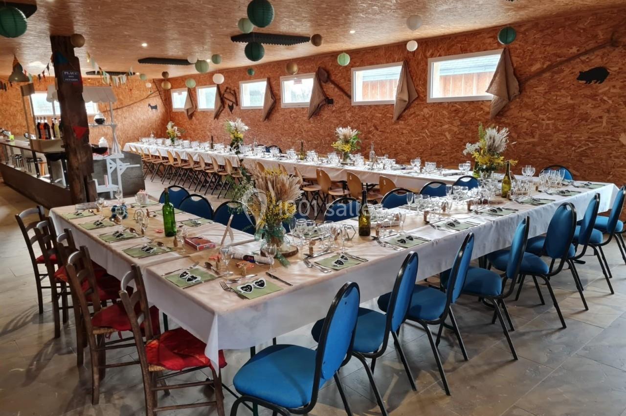 Salle décorée avec de longues tables dressées pour un repas, ornées de bouquets champêtres et de vaisselle.