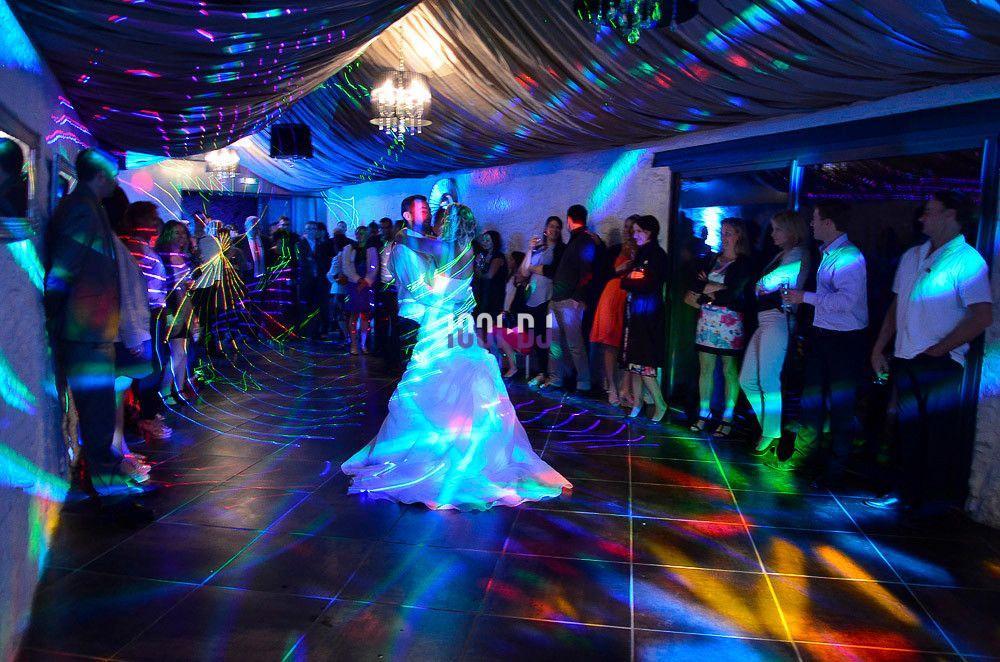 Un couple danse au centre d'une salle éclairée par des lumières colorées, entouré d'invités debout.
