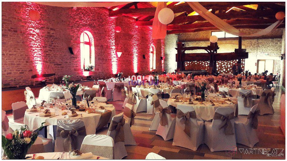 Salle de réception décorée pour un mariage, avec tables rondes dressées, nappes blanches et éclairage chaleureux.