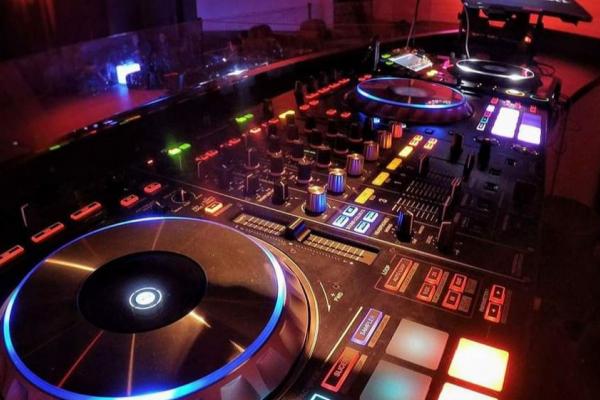 Table de mixage DJ éclairée avec des boutons, des curseurs et des platines lumineuses dans un environnement sombre.