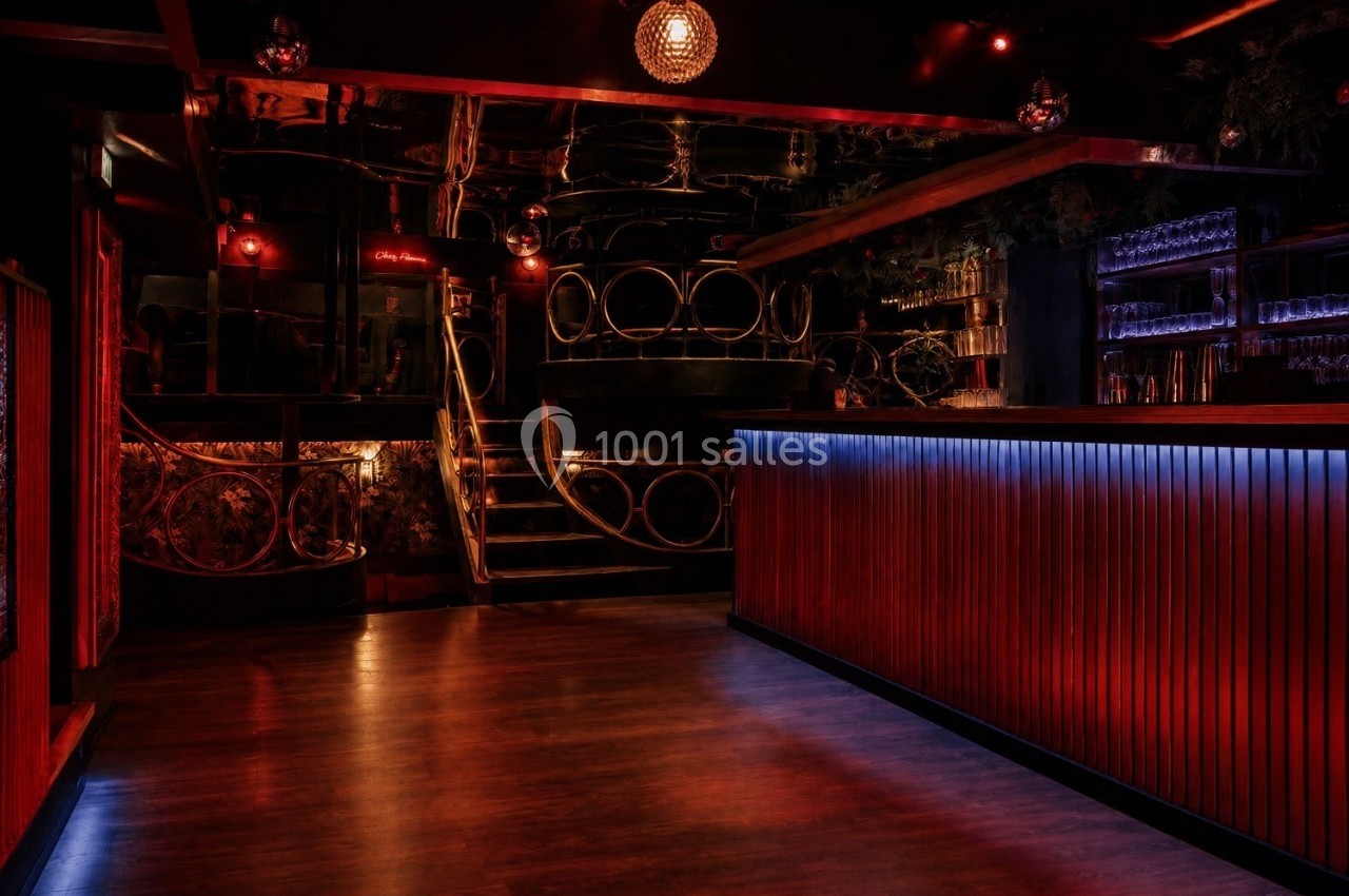 Intérieur d'un bar sombre avec éclairage rouge, comptoir en bois illuminé et escalier décoratif en arrière-plan.