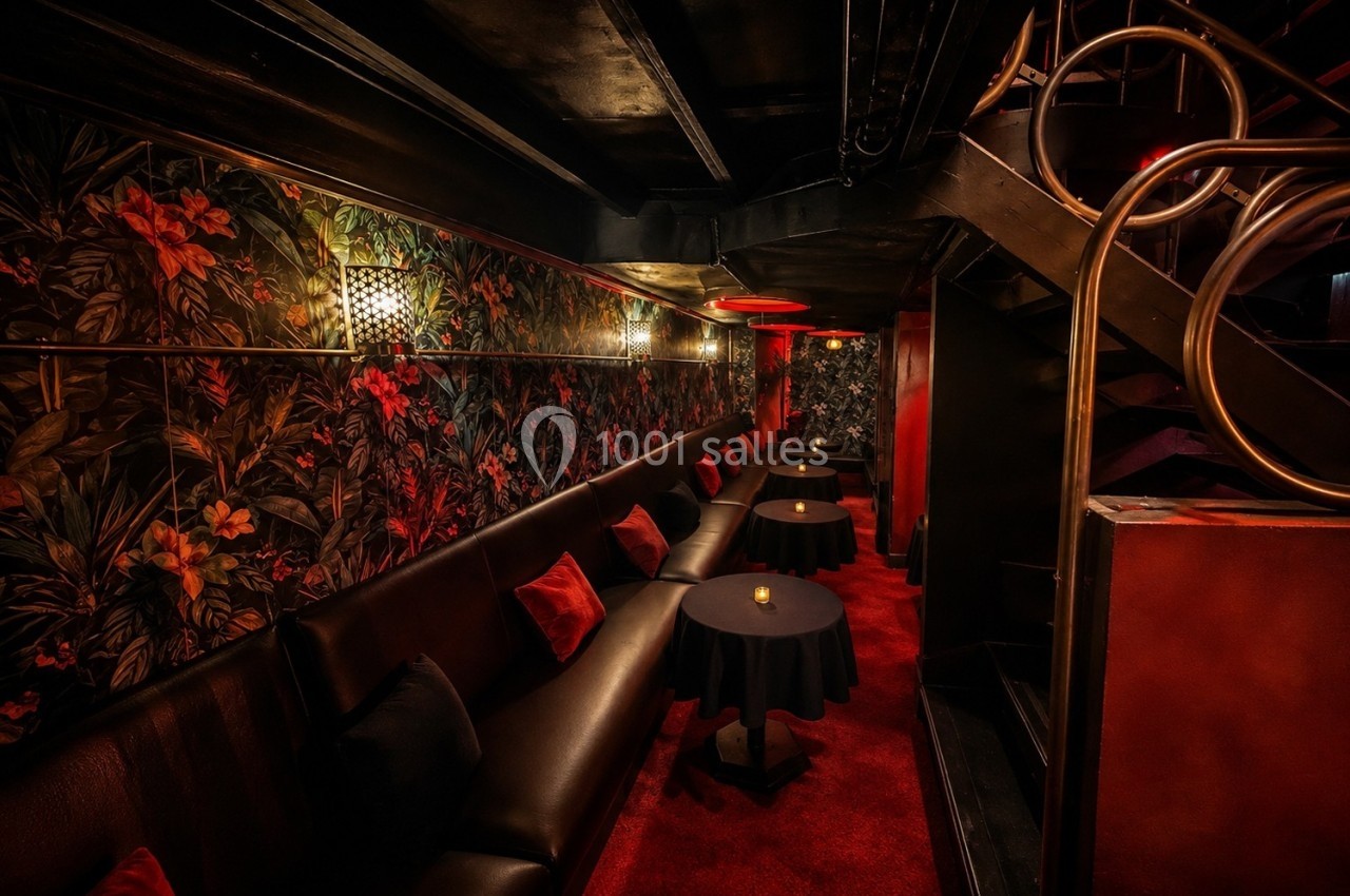 Banquette en cuir noir, tables rondes et décor mural floral dans un espace intérieur à l'éclairage tamisé.