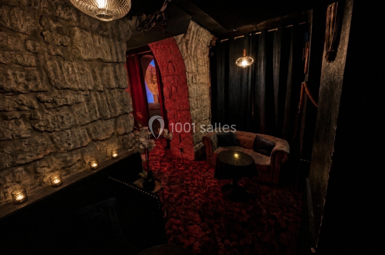 Salon intimiste avec murs en pierre, éclairage tamisé, canapé, table basse et rideaux sombres.