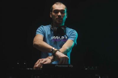 Portrait d'un homme souriant avec un éclairage tamisé sur fond sombre, un logo ’1001 DJ’ superposé au centre.