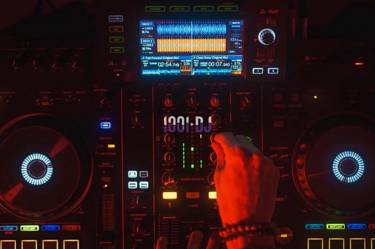 Main d'une personne ajustant les commandes d'une console de mixage DJ éclairée par des lumières colorées.