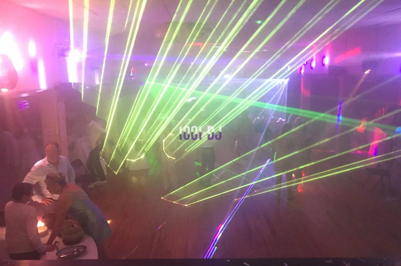 Des faisceaux laser colorés illuminent une salle sombre où des personnes discutent et se déplacent.