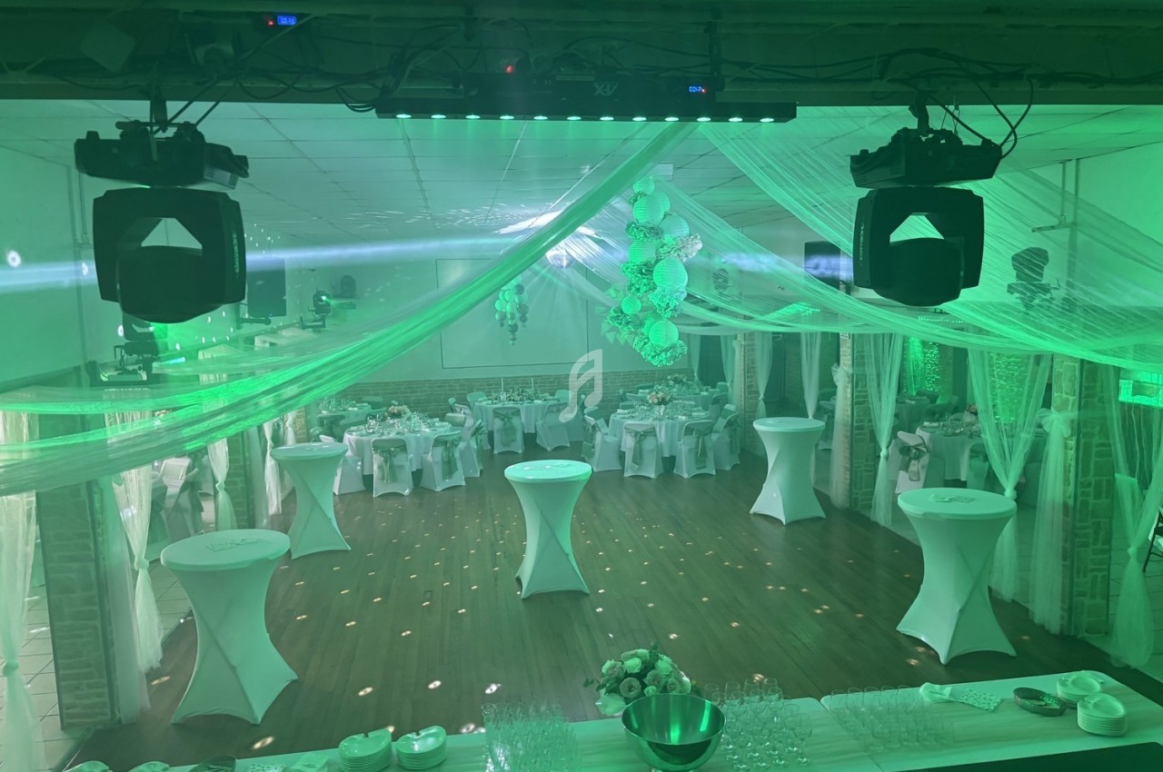 Salle de réception décorée avec des nappes blanches, des tables hautes et un éclairage vert diffus.