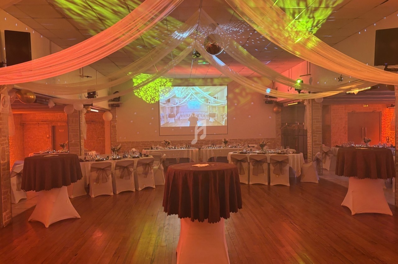 Salle de réception décorée avec des tables dressées, des drapés suspendus et un éclairage coloré.