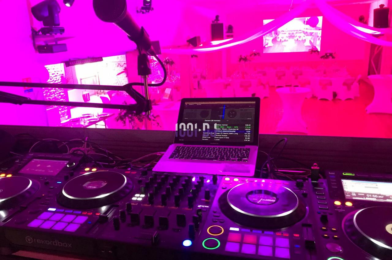 Table de mixage DJ avec platines, microphone et ordinateur portable dans une salle éclairée par des lumières roses.
