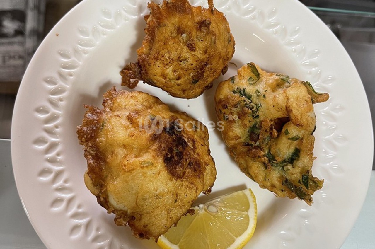 Beignets dorés sur une assiette blanche, accompagnés d'un quartier de citron.