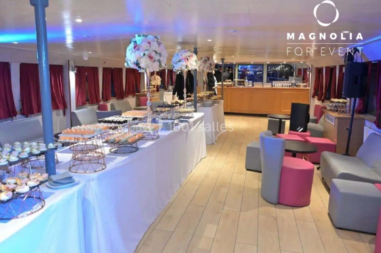 Salle de réception sur un bateau avec tables dressées, décorations florales et éclairage tamisé.