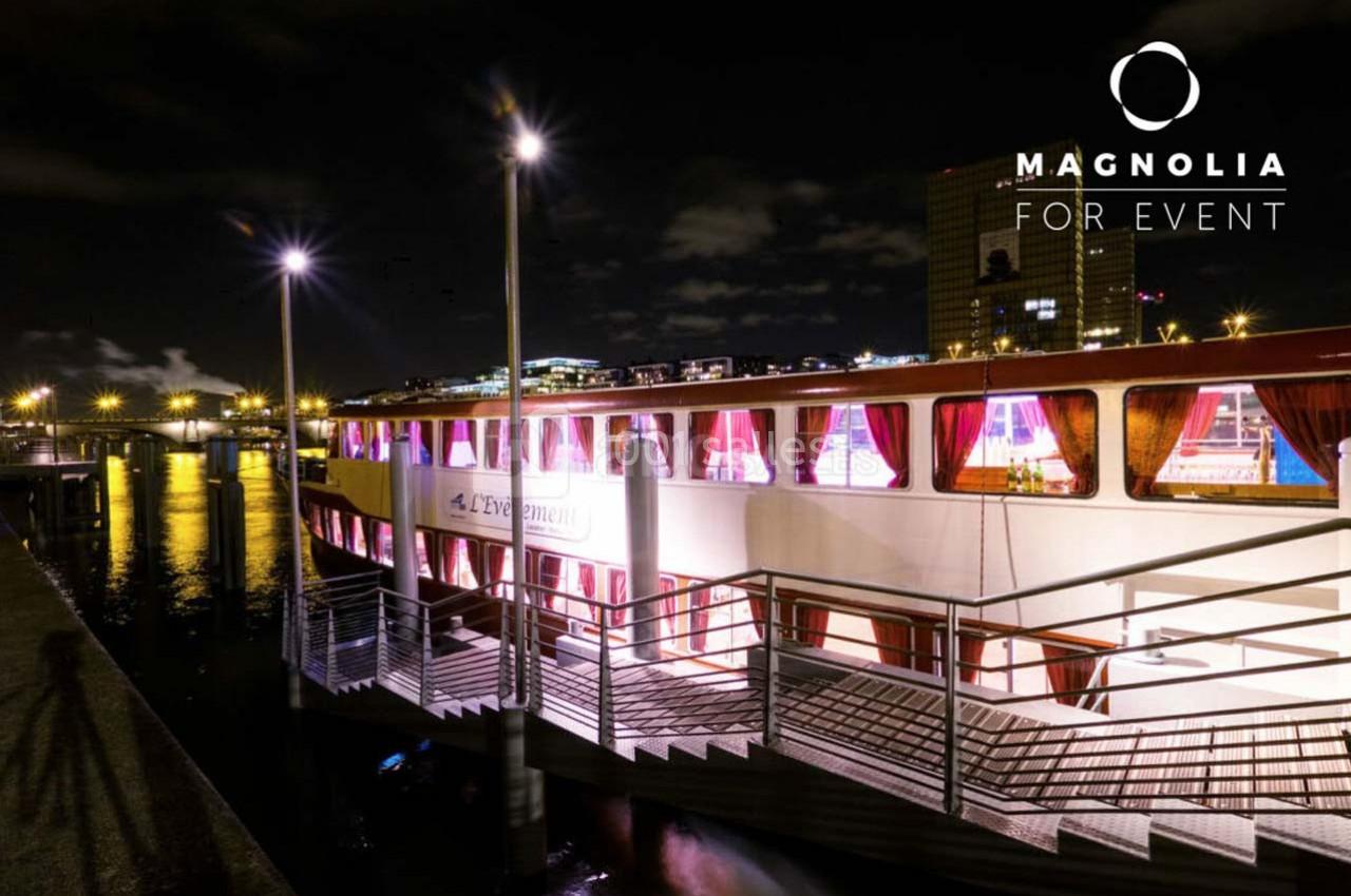 Bateau éclairé amarré de nuit près d'un quai, avec des lumières reflétées sur l'eau.