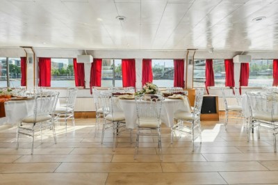 Miniature Location salle Paris 12 (Paris) - La Péniche Croisière de Bercy #7 Intérieur d'une salle spacieuse avec parquet, canapés colorés, tables rondes noires et rideaux rouges.