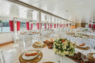 Miniature Location salle Paris 12 (Paris) - La Péniche Croisière de Bercy #8 Intérieur d'une salle spacieuse avec parquet, canapés colorés, tables rondes noires et rideaux rouges.
