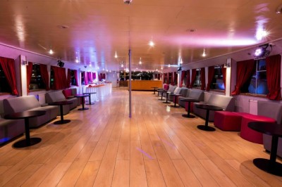 Miniature Location salle Paris 12 (Paris) - La Péniche Croisière de Bercy #12 Intérieur d'une salle spacieuse avec parquet, canapés colorés, tables rondes noires et rideaux rouges.