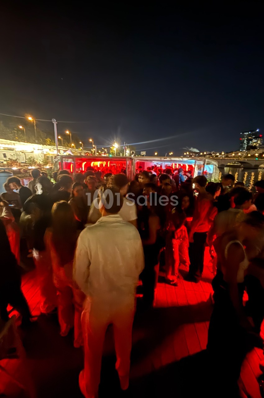 Groupe de personnes rassemblées sur une terrasse extérieure éclairée par des lumières rouges, de nuit.