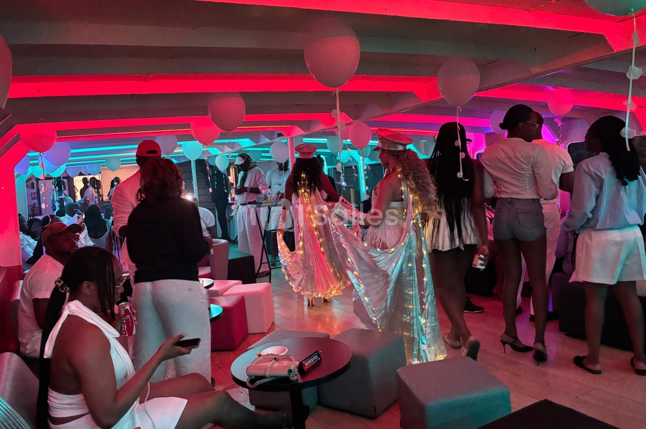 Personnes en tenue blanche et festive dans une salle éclairée de lumières rouges et bleues, décorée de ballons.