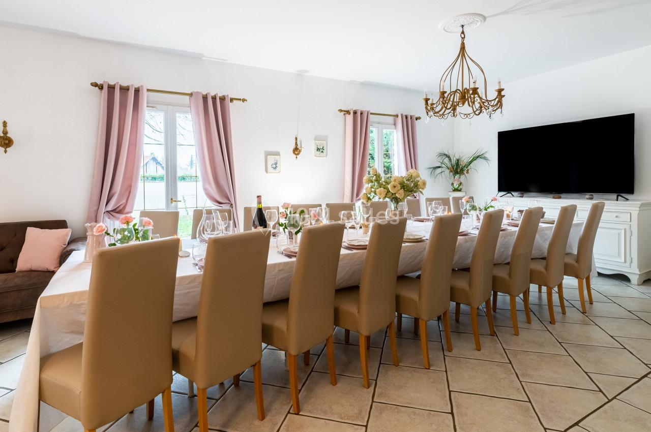 Grande table dressée avec vaisselle élégante dans une salle lumineuse, décorée de rideaux roses et d'un lustre doré.