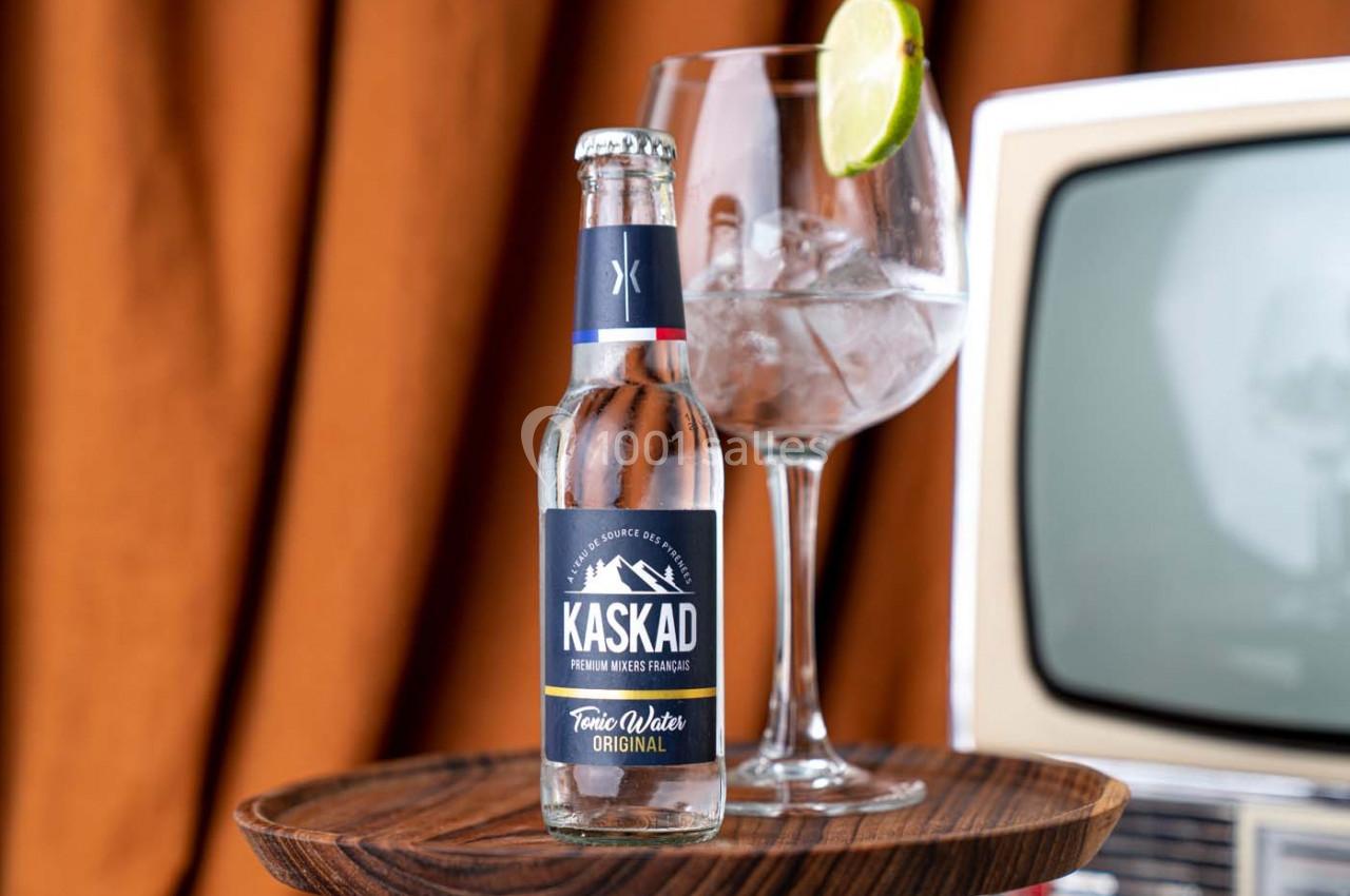 Bouteille de tonic sur une table en bois, accompagnée d'un verre de cocktail garni d'une rondelle de citron vert.