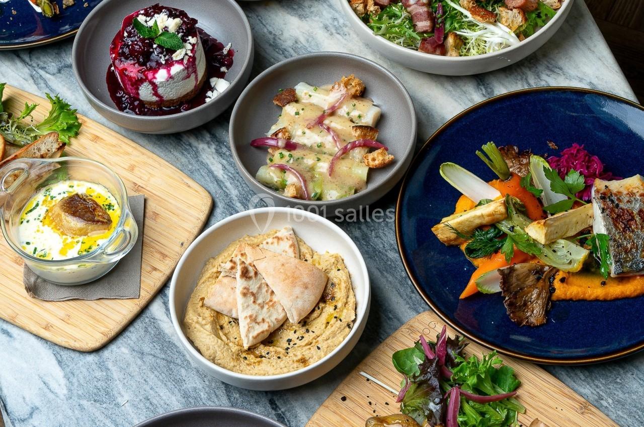 Table garnie de plats variés : légumes grillés, viandes, fromages, houmous, pommes de terre et salades colorées.