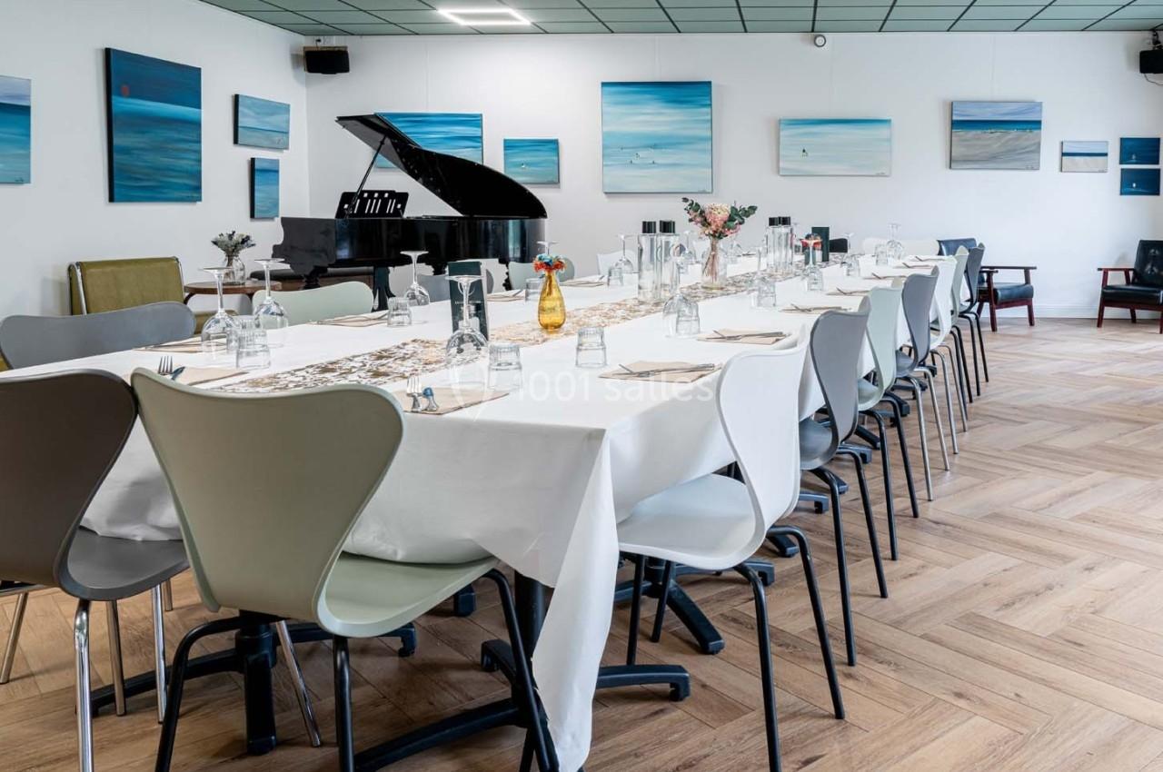 Salle de réception avec une longue table dressée, des chaises modernes et un piano à queue en arrière-plan.