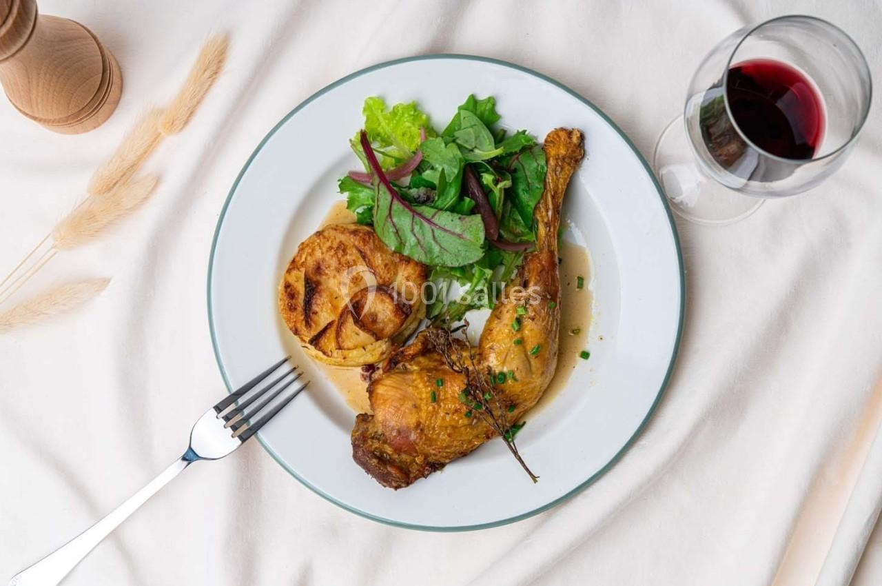Assiette contenant une cuisse de volaille rôtie, des pommes de terre gratinées, une salade verte et un verre de vin rouge.