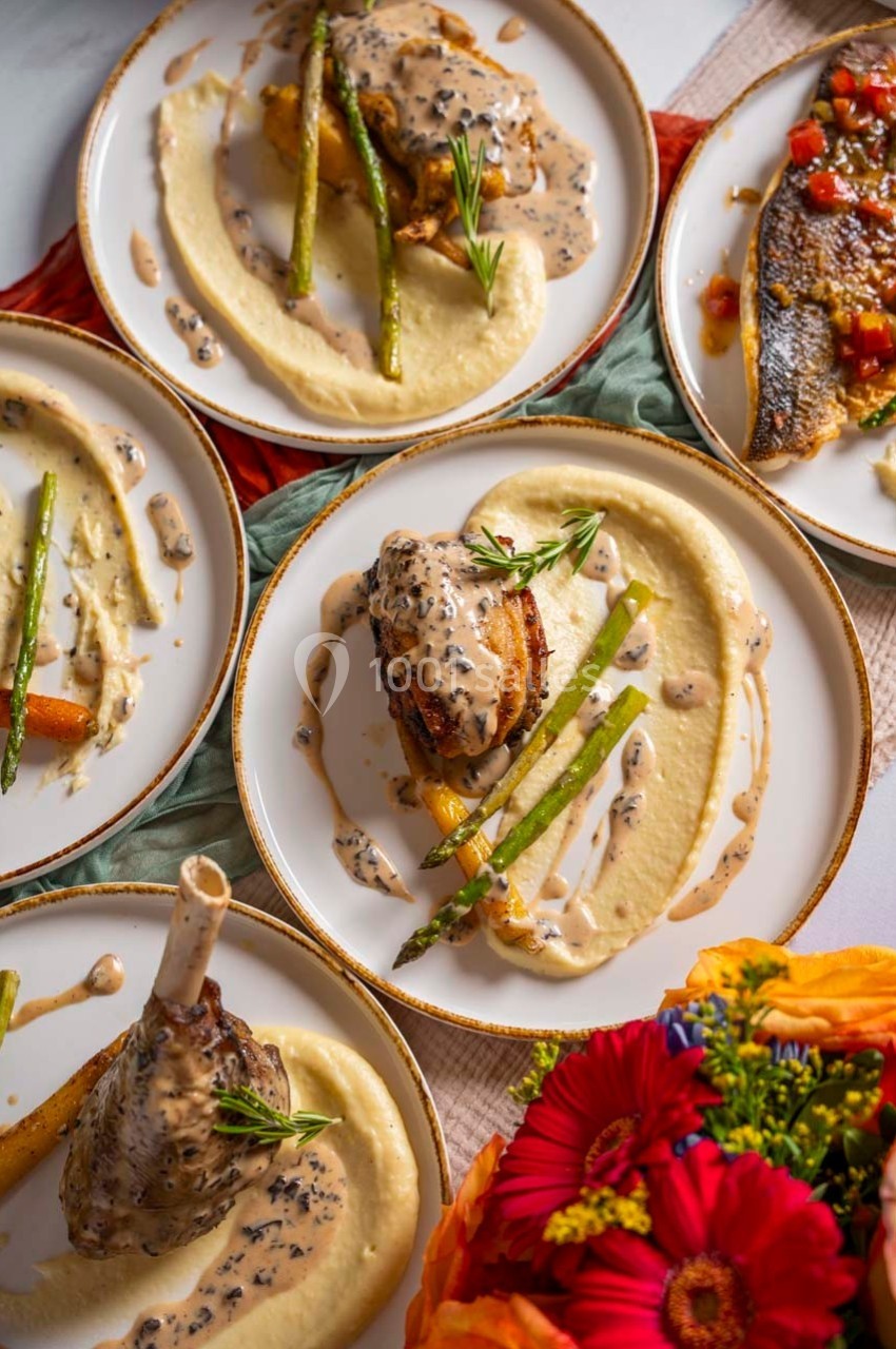 Assiettes garnies de viande, purée, asperges et sauce crémeuse, entourées de fleurs et de nappes colorées.