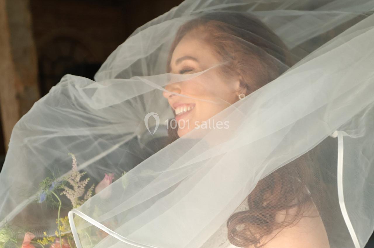 Femme souriante portant un voile de mariée translucide, tenant un bouquet de fleurs colorées.