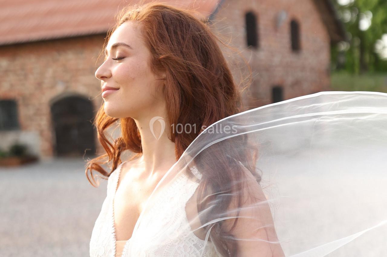Femme aux cheveux roux portant une robe blanche, debout à l'extérieur près d'un bâtiment en briques.