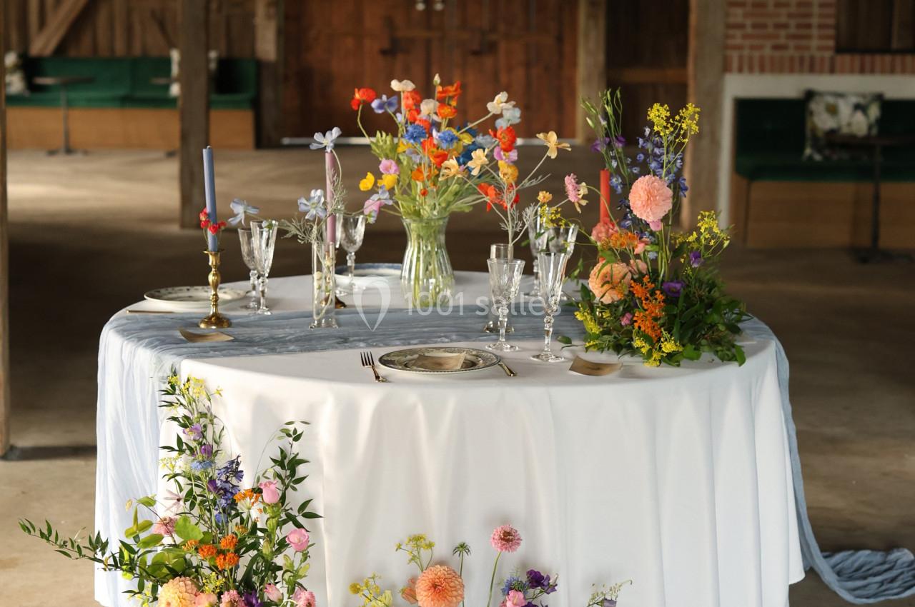 Table ronde décorée de fleurs colorées, bougies et vaisselle élégante dans un espace intérieur rustique.