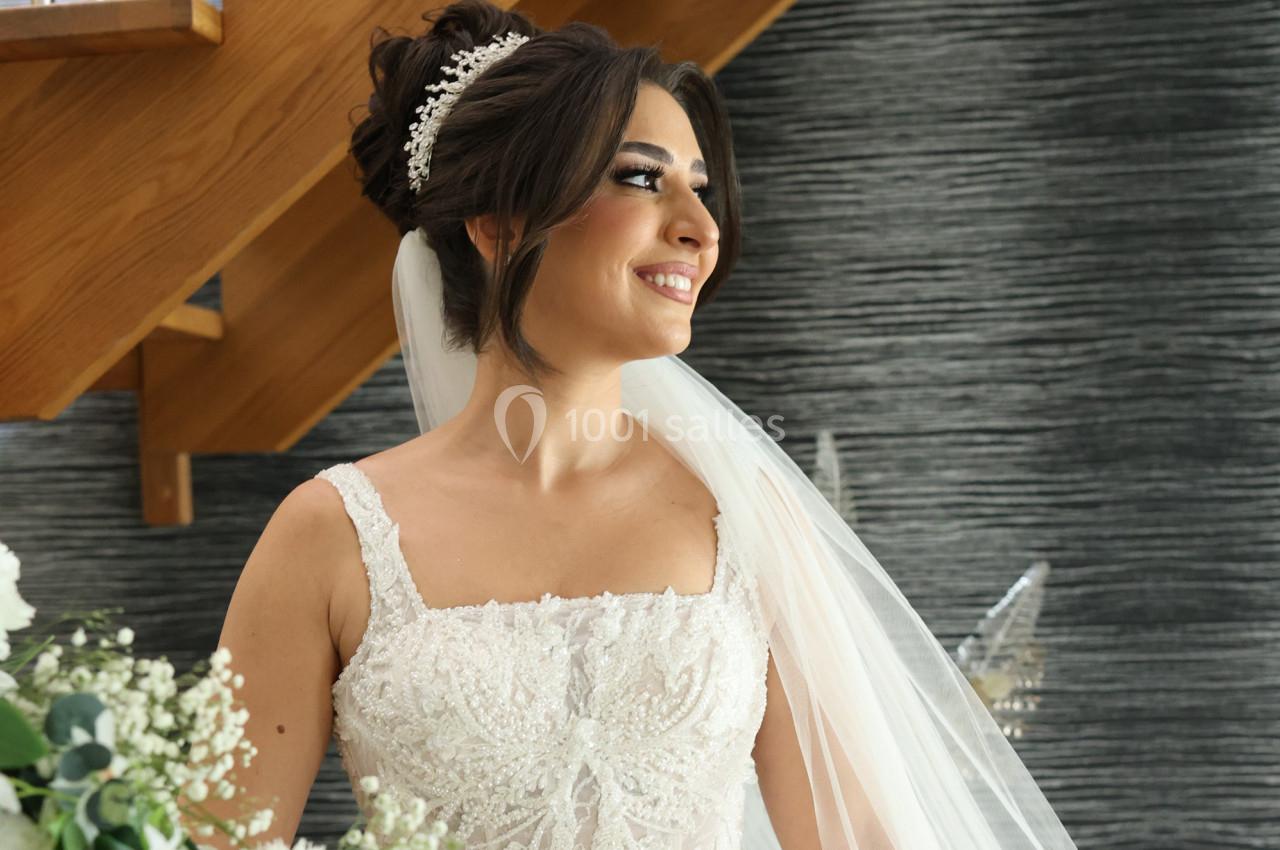 Femme en robe de mariée blanche ornée de dentelle, portant un voile et un accessoire dans les cheveux, souriante devant un…