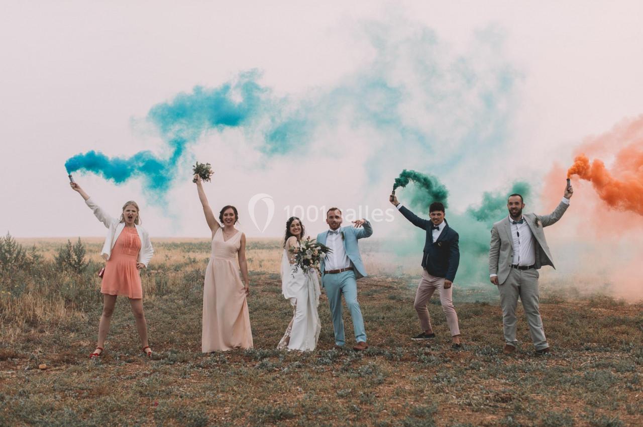 Un groupe de personnes en tenue de cérémonie tient des fumigènes colorés dans un champ ouvert.
