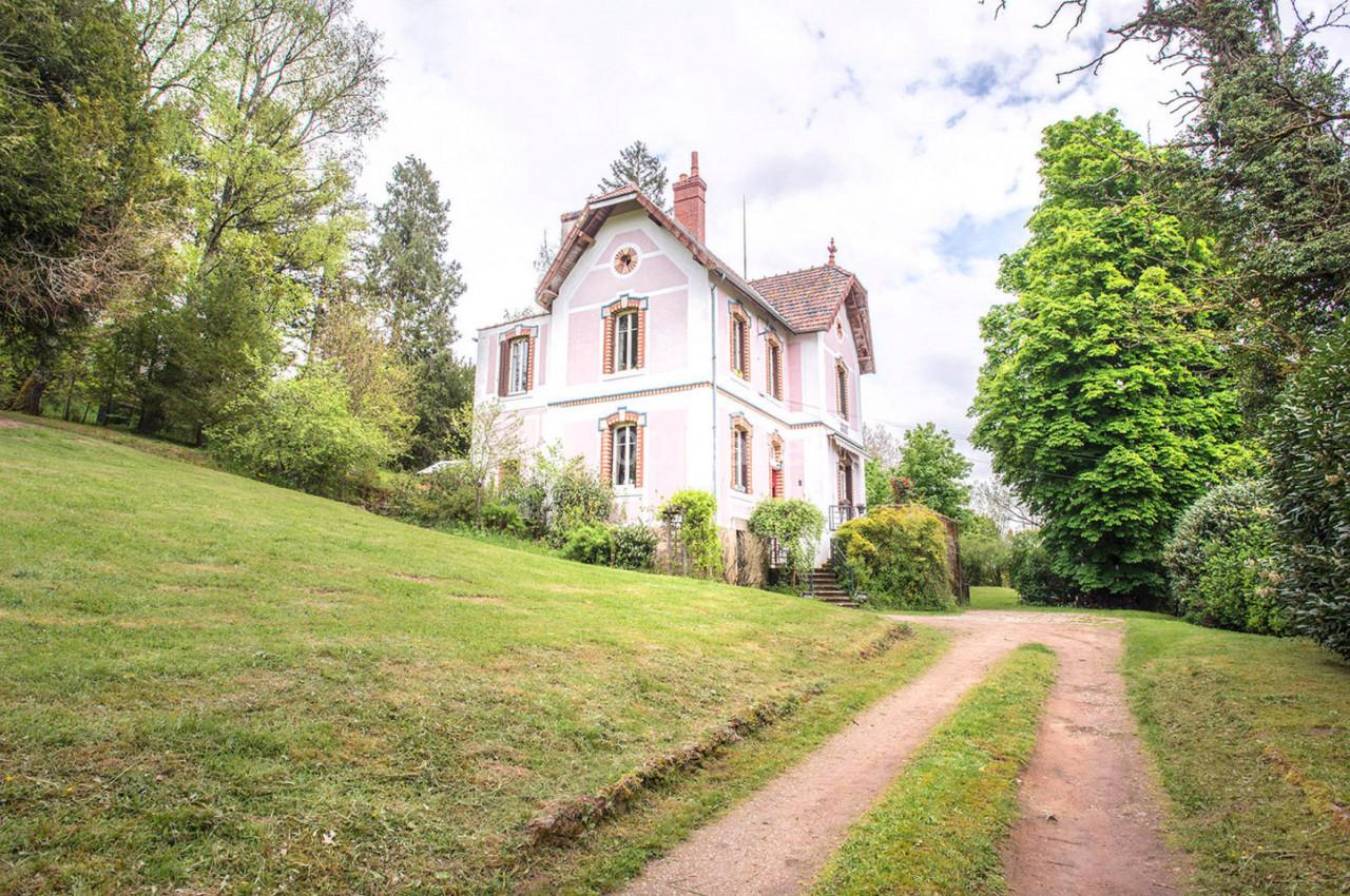 Maison blanche à deux étages avec toit en tuiles, entourée d'un jardin verdoyant et d'un chemin en terre.