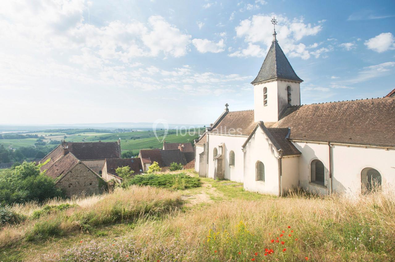Église rurale entourée de maisons et de champs verdoyants sous un ciel dégagé.