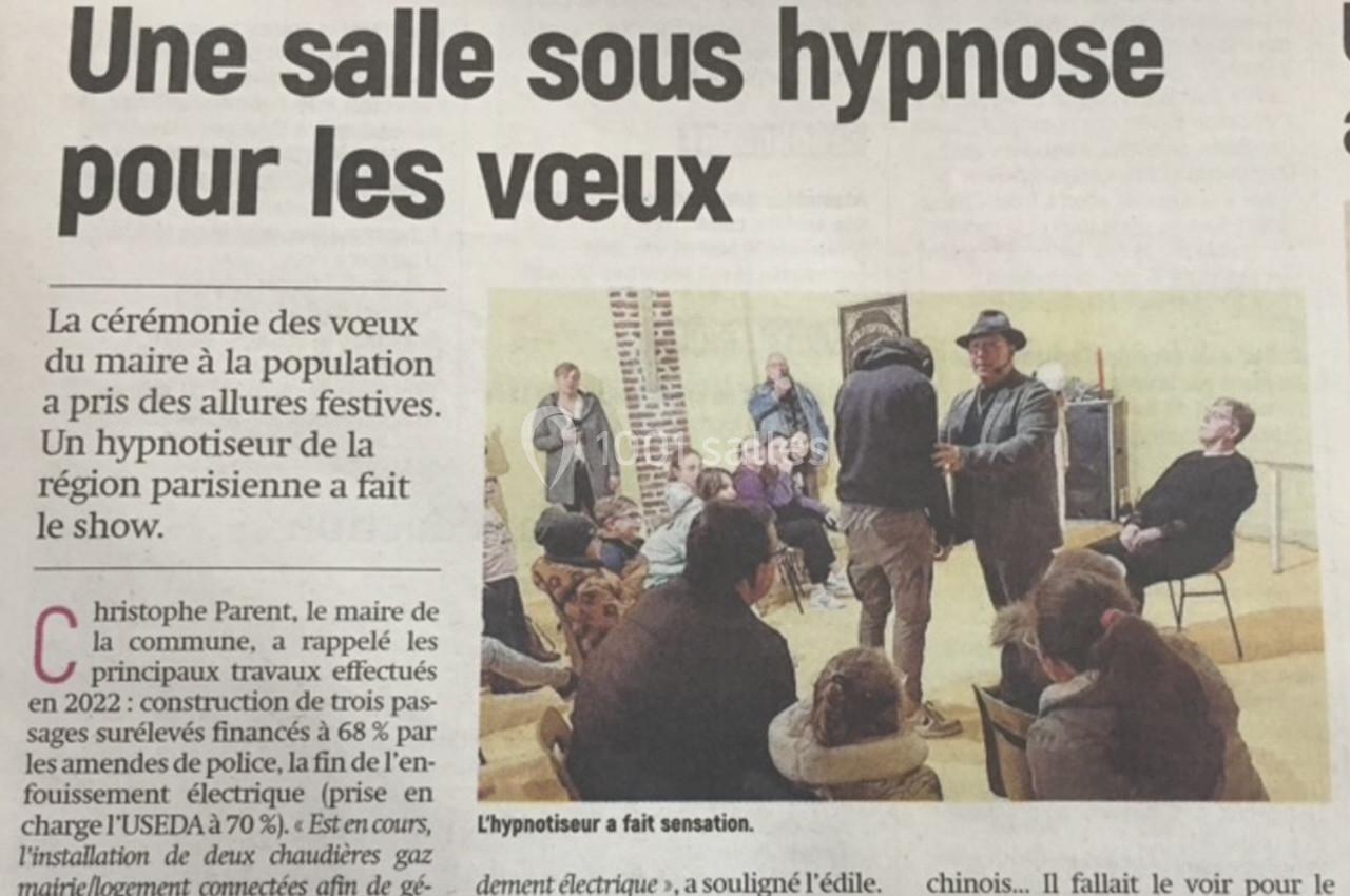 Un hypnotiseur anime une séance devant un public assis dans une salle, dans le cadre d'une cérémonie officielle.