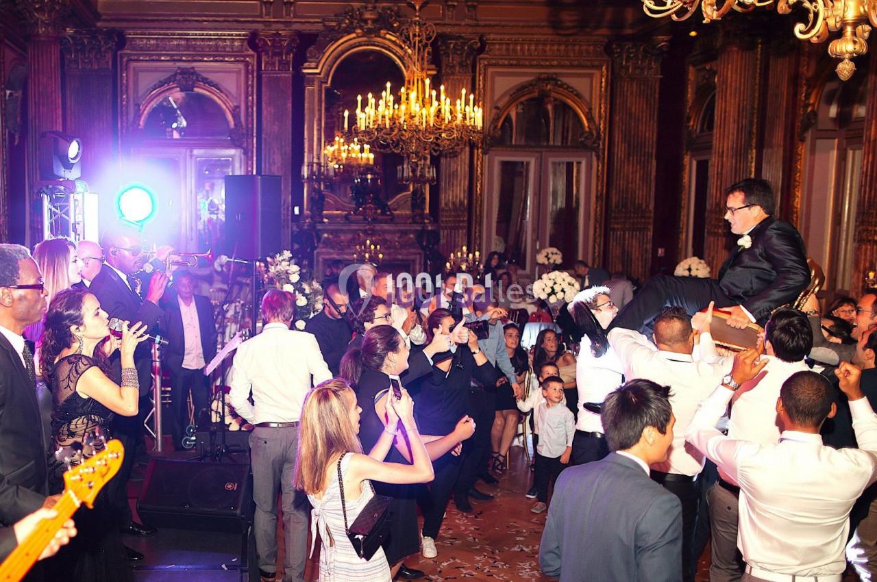 Groupe de personnes dans une salle élégante avec lustres, dansant et célébrant lors d'un événement festif.