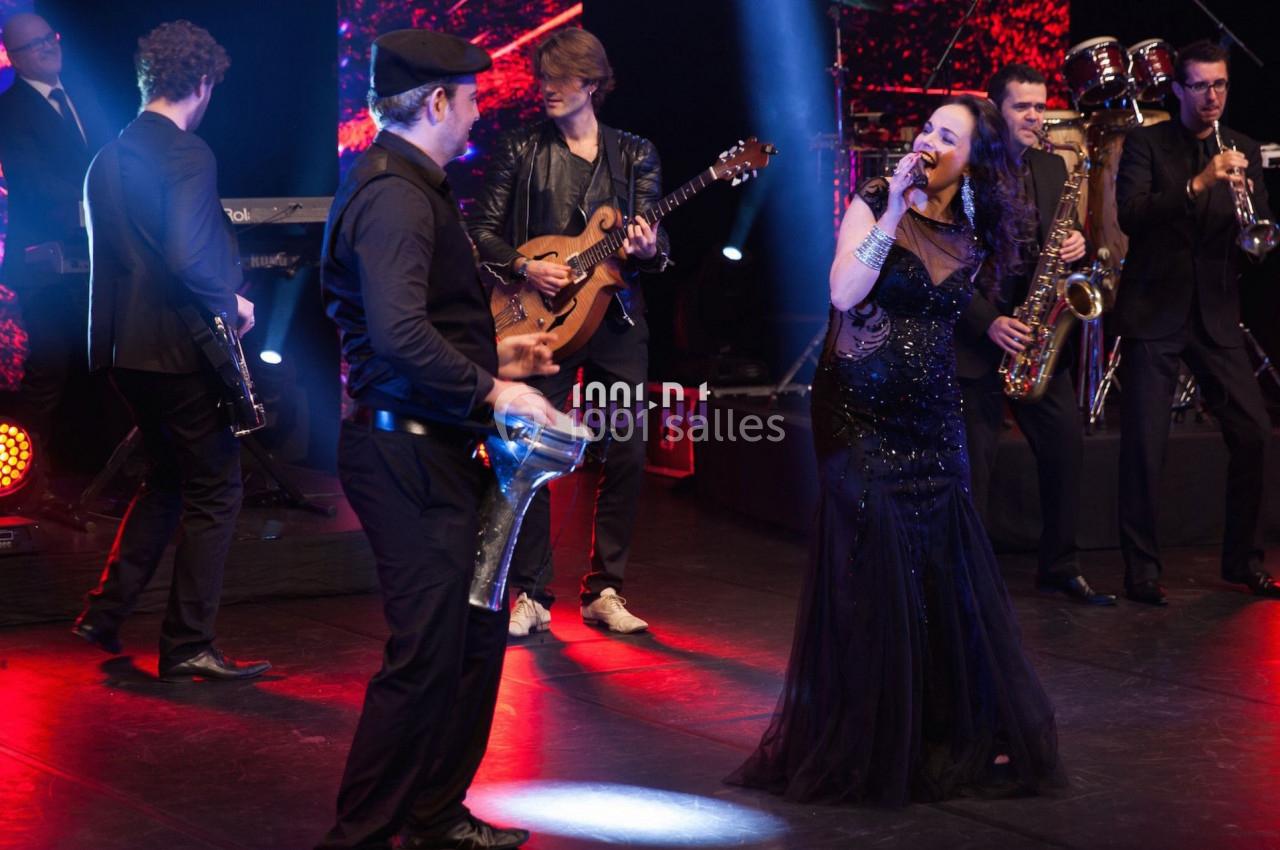 Un groupe de musiciens et une chanteuse se produisent sur scène avec des éclairages rouges et noirs.